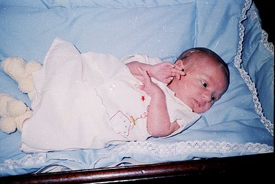 Vintage newborn portrait in a vintage-style wooden crib with lace trim, dressed in a white onesie with a cartoon character ap...