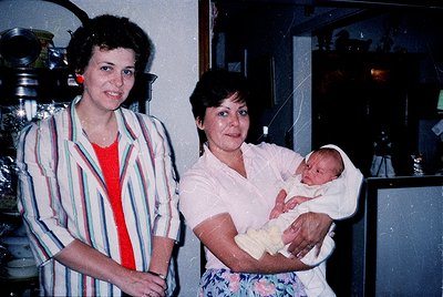 Vintage indoor portrait featuring two women and a newborn in a domestic setting, likely mid-1970s–1980s. The woman on the lef...