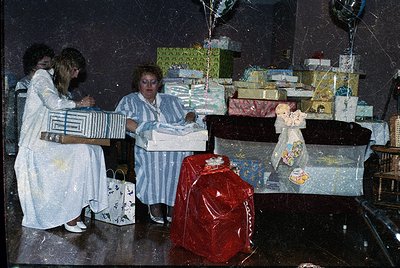 Vintage holiday scene featuring three women in 1970s-style housecoats wrapping gifts. Stacked presents in colorful paper surr...