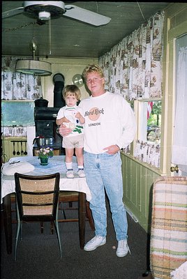 Vintage 1970s interior shot: man in a **Hard Rock Café London** sweatshirt poses with a toddler in a retro kitchen. Wooden ta...