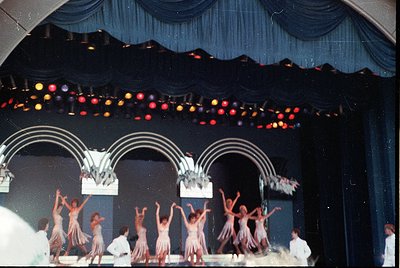 Vintage stage performance featuring a group of dancers in coordinated, flowing white costumes with red accents, performing un...