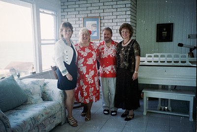 Four individuals pose indoors in a mid-century interior, likely 1970s–1980s. The woman on the left wears a structured blazer ...