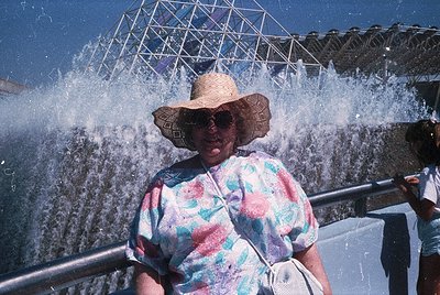 Vintage 1970s photo of a woman in a floral-patterned blouse and straw hat, posing near a massive fountain at the **Expo 70 Os...