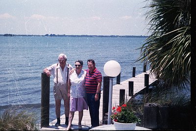Three adults pose on a seaside wooden pier, 1970s-80s. Elderly couple in retro swimwear (man in suspenders, woman in floral d...