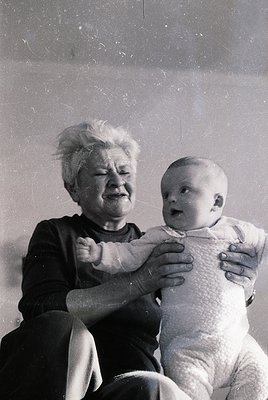 Black-and-white portrait of an elderly woman cradling an infant, likely mid-20th century. The woman’s expressive face and the...