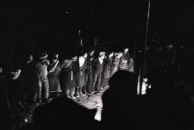 Black-and-white photo of a nighttime protest or demonstration, likely 1960s–1980s. Crowd of men in dark clothing, some holdin...