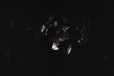 High-contrast black-and-white image of a group of people in a dimly lit, possibly indoor setting. Silhouetted figures appear ...