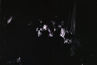 Vintage black-and-white photo of a crowded, dimly lit indoor gathering with silhouetted figures dancing. Dynamic poses sugges...
