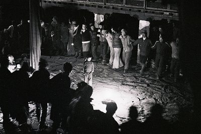 Black-and-white photo captures a lively 1970s dance scene in an indoor venue, likely a club or community hall. Crowd of ~30 p...