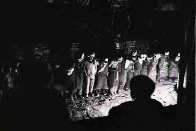 Black-and-white street scene featuring a crowd of men in 1960s–70s attire, likely Eastern European. Central figures wear suit...