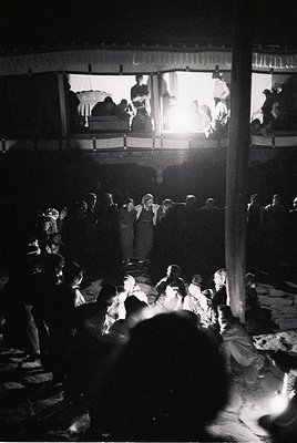 Vintage black-and-white shot of a packed open-air theater, likely 1950s–1960s. Stage lighting illuminates performers on an el...