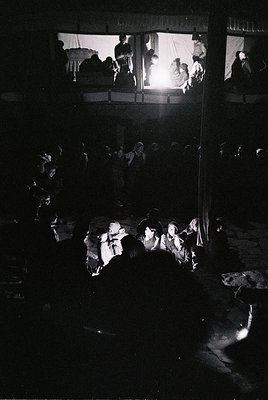 Vintage black-and-white photo of a dimly lit, two-tiered gathering with silhouetted figures. Lower level: small group huddled...