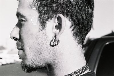 Close-up portrait of a bearded man with a spiral earring, captured in black-and-white. His short, textured hair and focused g...