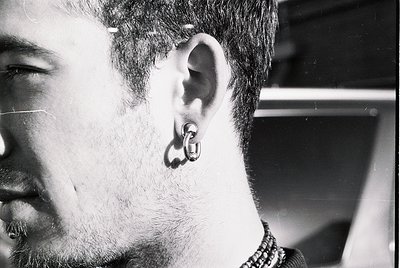 Close-up of a bearded man with a distinctive **hoop earring** in his left ear, captured in black-and-white. The texture of hi...