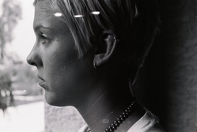 Portrait of a young woman in profile, captured in black-and-white. She wears a pearl necklace and a short, layered hairstyle....