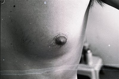Close-up of a male chest with a prominent nipple and surrounding hair, captured in black-and-white. The texture suggests aged...