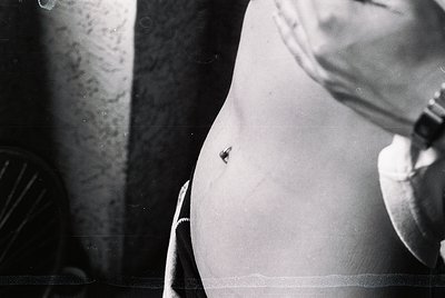 Close-up of a vintage black-and-white photograph showing a pregnant belly with a small, visible button or pin. The grainy tex...