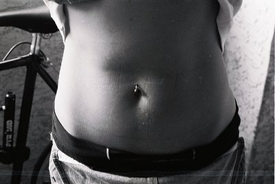 Black-and-white close-up of a child’s torso, mid-growth stage, seated near a bicycle frame. Minimalist composition highlights...