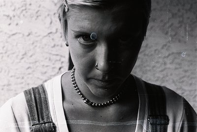Close-up portrait of a person with a piercing nose ring and earring, wearing a beaded necklace. The striped fabric and textur...