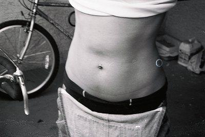 Close-up of a person’s torso seated on a vintage bicycle seat, wearing a white cap and loose-fitting pants. Industrial settin...