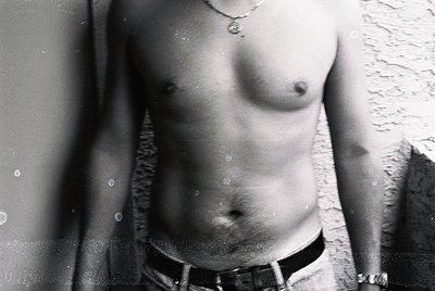 Black-and-white close-up of a shirtless male torso, wet with droplets, against a textured wall. Minimalist composition highli...