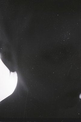 High-contrast black-and-white portrait of a person’s face in profile, backlit by a bright light source. Skin texture and subt...