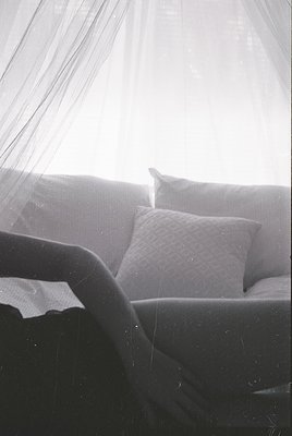 Minimalist black-and-white interior shot featuring a low-profile sofa with tufted backrest, draped in soft fabric. Sunlight s...