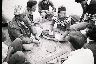 Group of men seated on floor playing traditional board game, likely in South Asia. Mid-20th century attire suggests or . Dist...