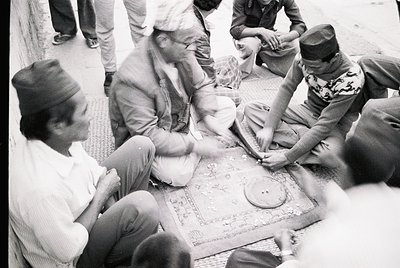 Group of men playing traditional board game on patterned rug, mid-20th century. Indoor setting with blurred background, sugge...