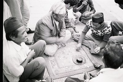 Group playing traditional board game on woven mat, likely backgammon, in 1960s-70s Middle East. Men in traditional headwear a...