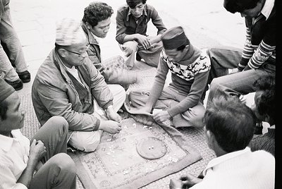 Black-and-white photo of a group playing a traditional board game in a communal setting, likely . Men in traditional attire (...