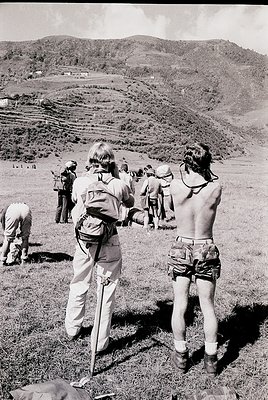 Group of hikers in 1970s-style outdoor gear stands on a terraced hillside, likely in a Mediterranean or alpine region. Shorts...