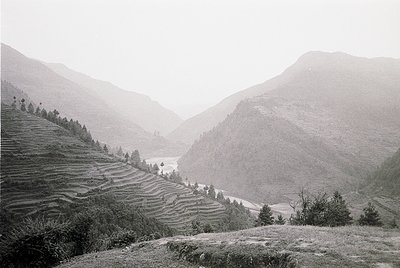 Terrace farming carved into steep slopes alongside a misty valley, framed by rugged mountains. Black-and-white vintage aesthe...