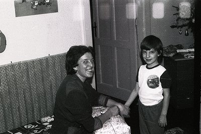 Black-and-white indoor portrait of a woman and young boy shaking hands, likely mid-1970s–1980s. Woman wears a dark blouse wit...