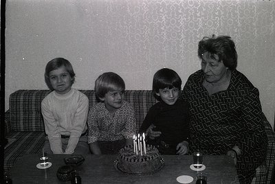Family portrait from the 1970s–1980s, likely Eastern Europe. Three children and an adult woman pose indoors beside a round bi...