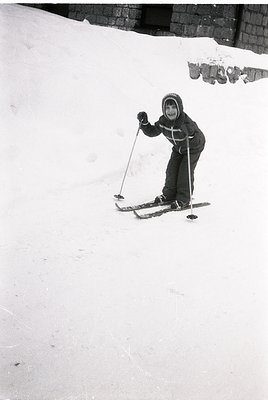 Child in vintage ski gear mid-turn on groomed slope, 1960s-70s style. Hooded jacket with cross patch, classic wooden skis, an...