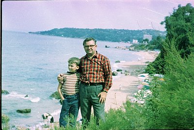 Vintage seaside portrait of a man in a plaid shirt and a young boy in striped shirt, posing on a grassy cliffside by the Blac...