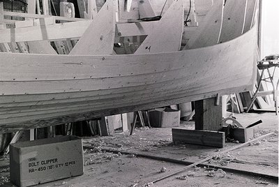 Mid-20th century boat construction in progress, featuring plywood hull assembly with visible rivets and clamps. Box labeled "...