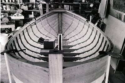 Traditional wooden boat under construction in a workshop, featuring curved planks and ribs. Industrial-era craftsmanship with...