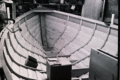 Traditional wooden boat under construction, showcasing curved planking and rib framework. Mid-20th century craftsmanship like...