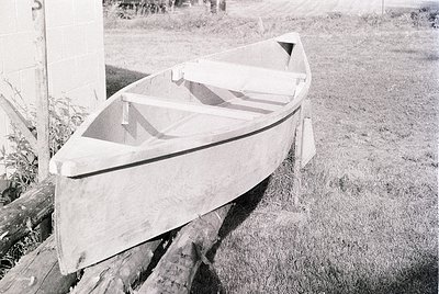 Handcrafted wooden rowboat resting on wooden supports, likely mid-20th century. Simple, functional design with minimalist lin...