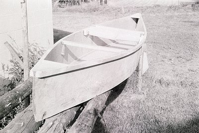 Classic wooden rowboat resting on wooden supports, likely mid-20th century. Smooth hull with simple, functional design, indic...