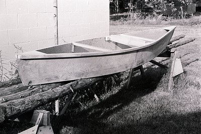 Handcrafted wooden boat on wooden supports, likely mid-construction or repair. Plain hull with minimal detailing, resting on ...