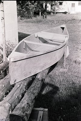Classic wooden dinghy resting on a wooden cradle, likely mid-20th century. Simple, functional design with a flat bottom and m...