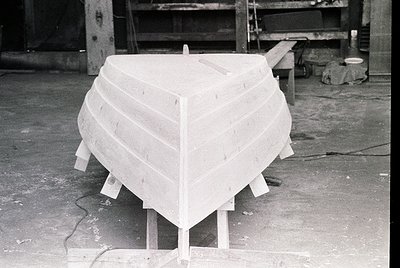 Unfinished wooden boat hull in a workshop, secured on wooden supports. Planking shows hand-cut seams, indicating traditional ...