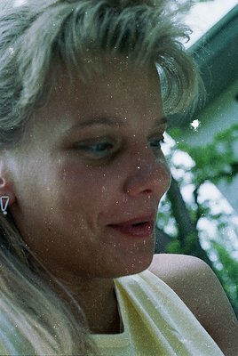 Close-up portrait of a woman with short, wavy blonde hair, captured mid-laugh or exhale. She wears minimalist white diamond s...