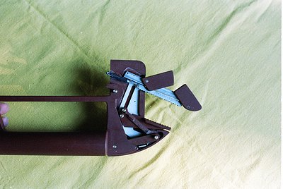 Close-up of a vintage **ski binding** with metal frame and adjustable toe piece, secured to a wooden ski. The binding’s rivet...
