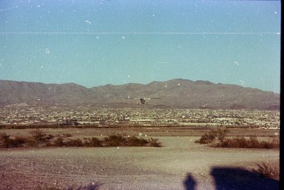 Vintage aerial shot of arid desert terrain with sparse vegetation, likely taken from a small aircraft. Distant mountains fram...