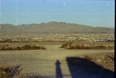 Vintage aerial view of arid landscape with sparse vegetation and distant mountain range. Urban sprawl visible below, suggesti...