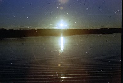 Sunburst reflection on calm waters, likely a lake or salt flat, with lens flare creating symmetrical light rays. The horizon ...